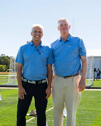 John Sorochan and John “Trey” Rogers III stand together on a field of grass.