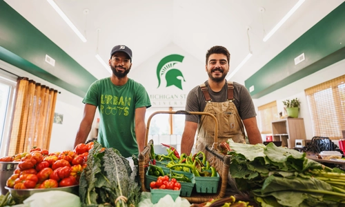 Two people standing behind stacks of produce