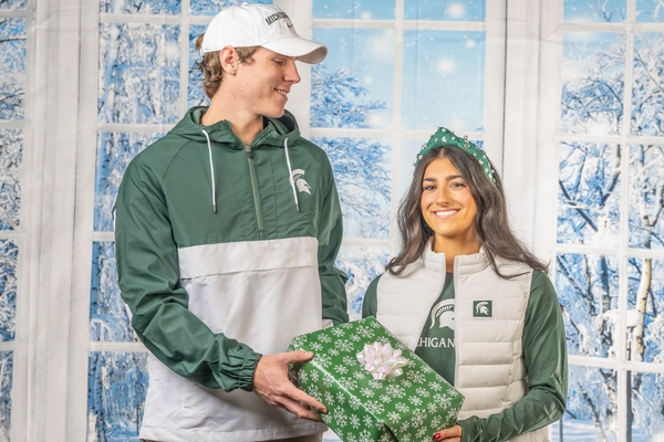Boy and girl smiling holding a wrapped gift in front of a winter backdrop